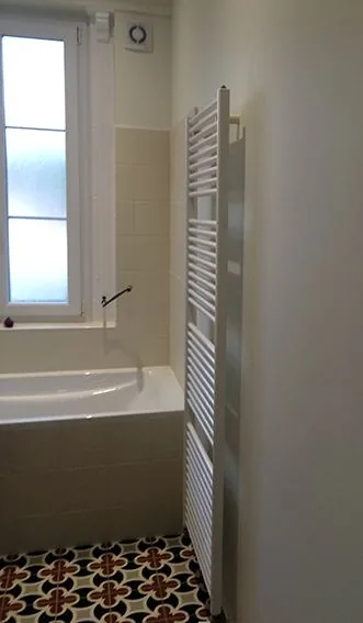 Salle de bains rénovée avec sèche-serviettes et baignoire